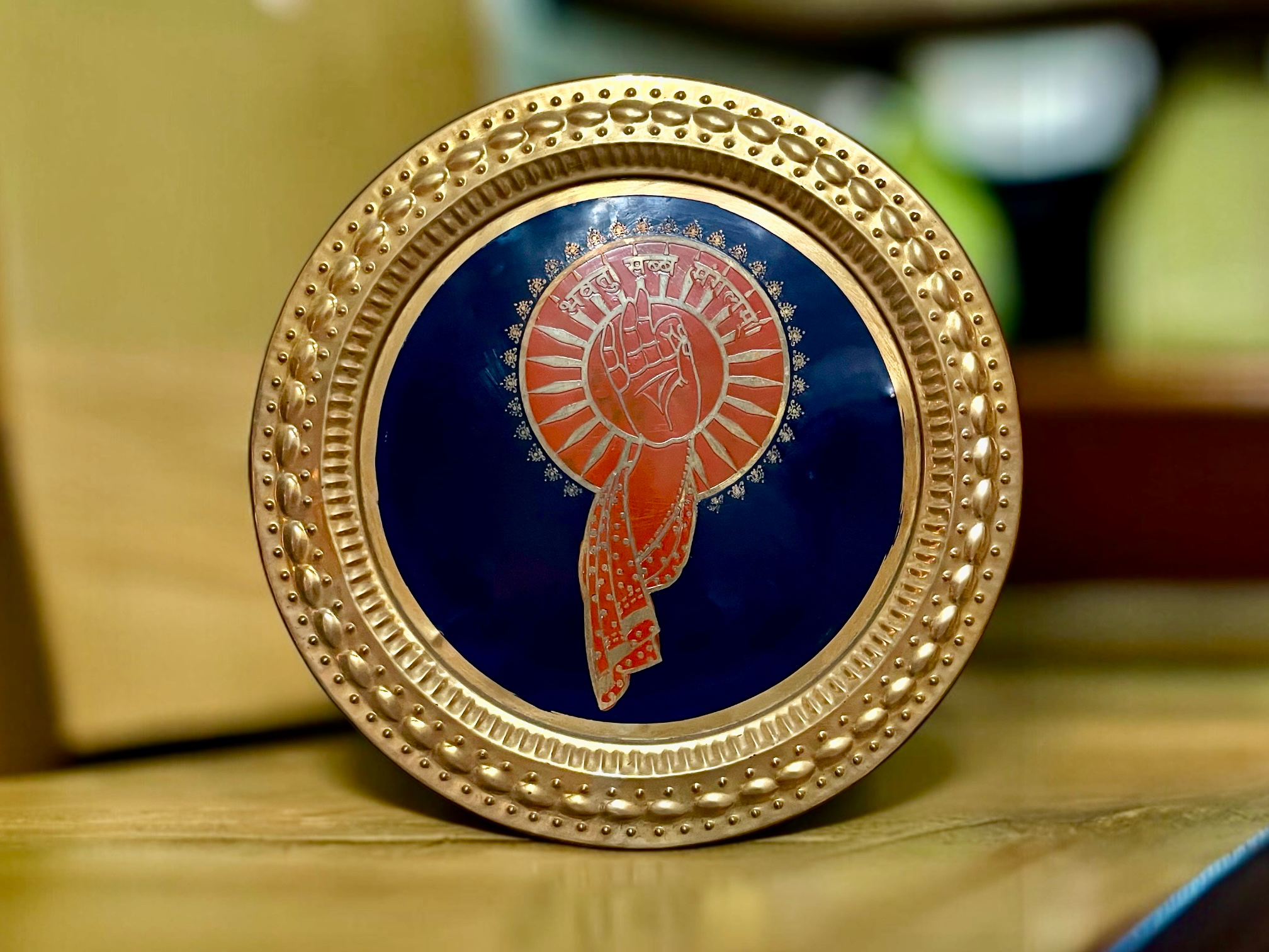 glenterprises handcrafted brass wall plaque with blue enamel and orange Jain Ahimsa symbol and textured gold border.